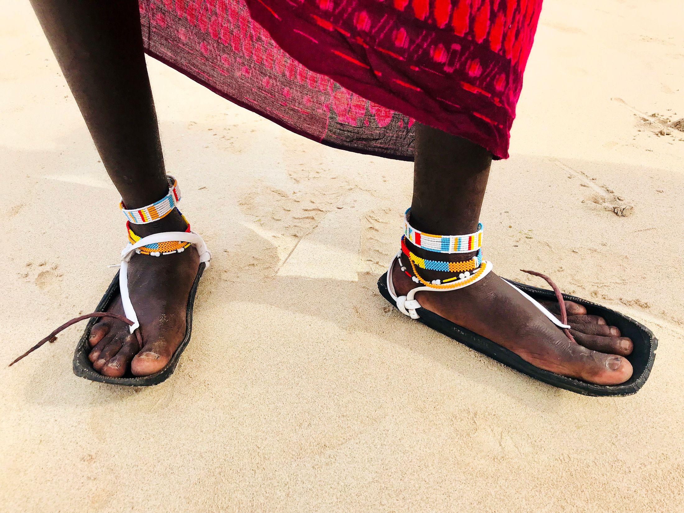Traditional black sandals and colourful anklets on a sandy beach